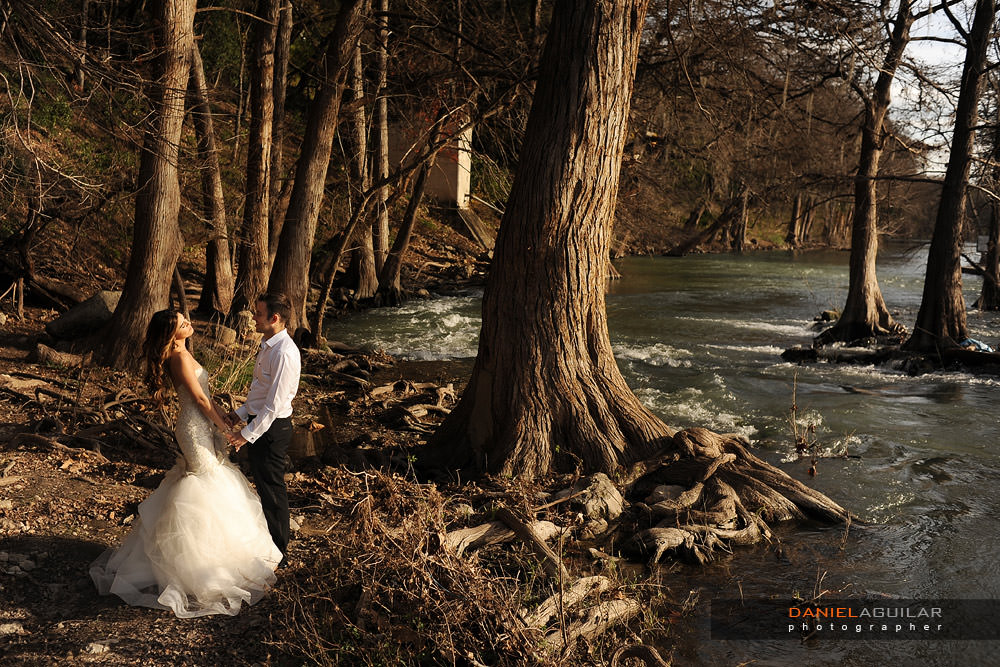 Bride and groom during trahs the dress session A bride and a groom holding hands at the shore of the Guadalupe River