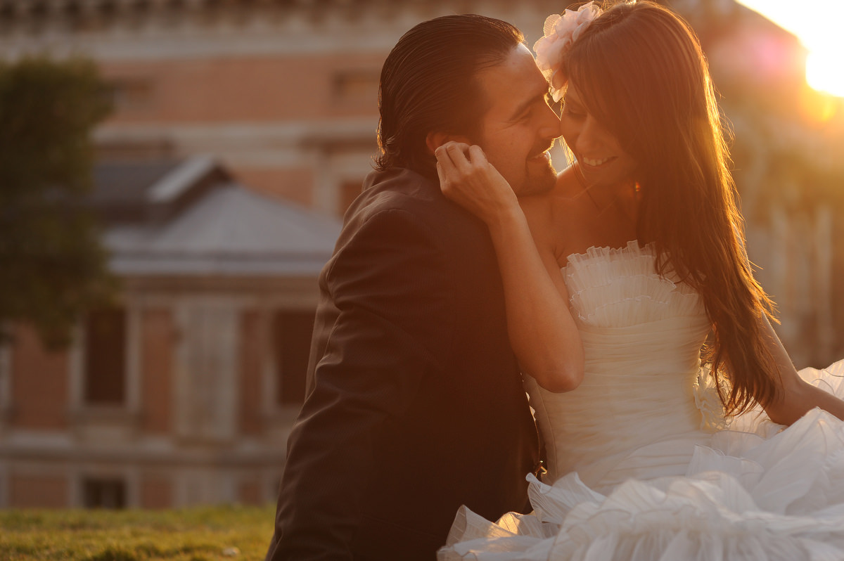 A bride and groom are smaling and laying in the ground outside the Prado Museum in Madrid, Spain. It is sunset time and the couple is shining with the last rays of light.