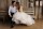 A bride and a groom are sitting down on a wooden bench and are smiling at each other during a trah the dress session in gruene texas