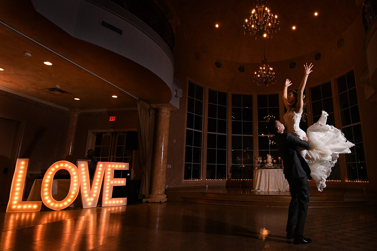 a bride is impresively help up in arms during a first dance while lit up letters with the word love are in the background during a first dance in chateau polonez houston