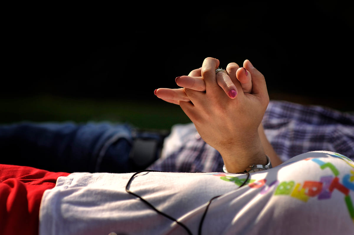 detail of two hands holding each other while a couple lays on the ground