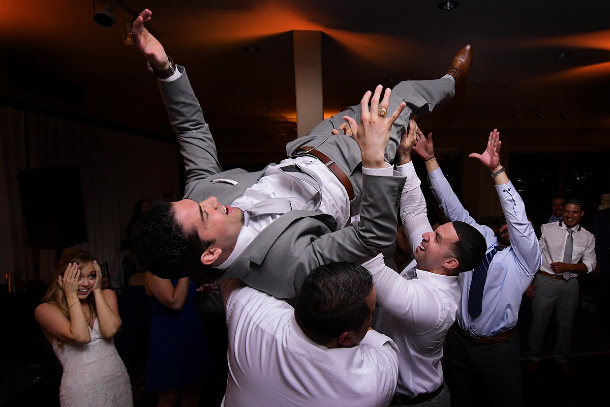 a groom is lifted up in arms by his friends while the bride is looking at the scene surprised during a wedding in zaza hotel in houston tx